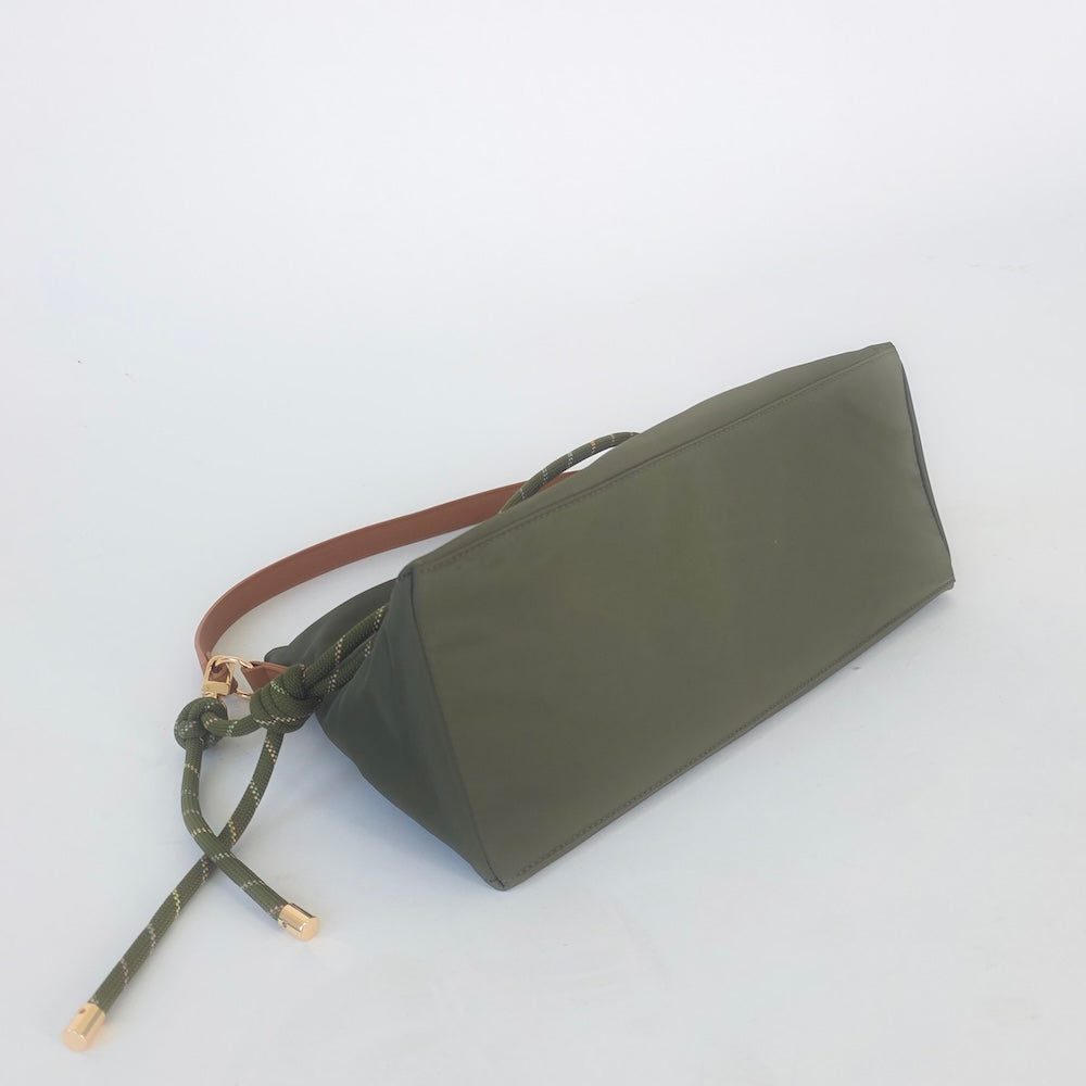 Digital photograph of an olive green fabric handbag on a white studio background, highlighting a tan leather strap and a thick knotted green rope with gold-toned metal tips