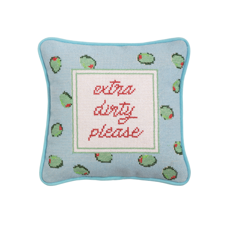 Needlepoint throw pillow by Furbish Studio featuring the phrase extra dirty please in red script centered amongst green pimento-stuffed olives on a light blue background with a piped edge