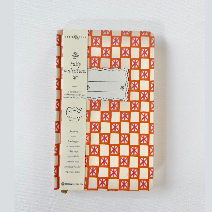 DesignWorks Ink and Paddywax journal featuring an orange and pink geometric pattern with stylized x-shapes, a white band displaying 'tulip collection', and a blank name label, highlighting features like lined pages and a celestial map