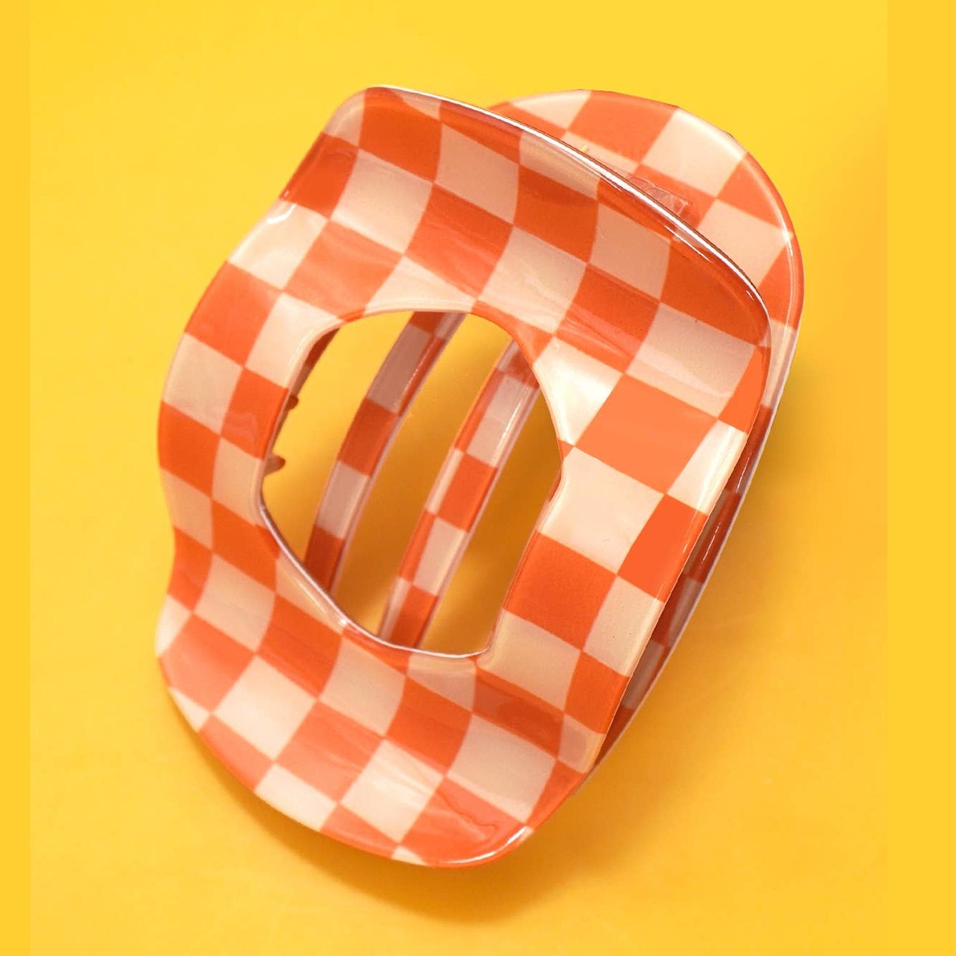 Translucent orange and white checkerboard pattern hair claw clip on a vibrant yellow background