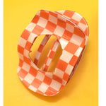 Orange and white checkered hair claw clip on a yellow background