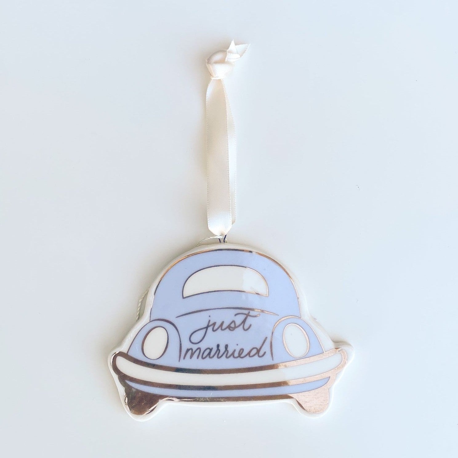 Ceramic ornament of a light blue vintage car with white bumpers and rose gold "just married" script hanging from a white ribbon
