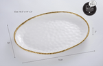 Pampa Bay porcelain oval serving platter with hammered texture, gold beaded rim, and dimensions 18.5 by 14 by 2 inches, prominently displaying its "It's Porcelain, I can't believe it's not metal!" branding in a studio setting
