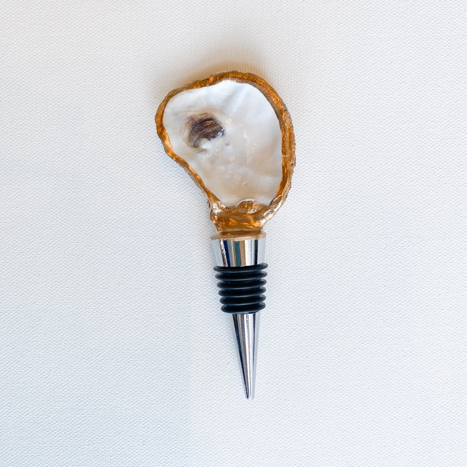 Handcrafted mixed media wine bottle stopper featuring a natural oyster shell with hand-painted gilded gold edges and a dark purple muscle scar atop a polished stainless steel base against a white textured background