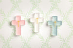 Three frosted glass crosses in pastel pink, white, and teal, each with an embossed golden cross, set against a white background with a repeating light green leaf pattern