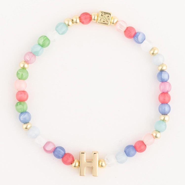 A vibrant pastel beaded bracelet featuring an array of pink blue green white and coral glass beads delicate gold spacer beads a unique gold engraved square charm and a prominent gold initial H charm