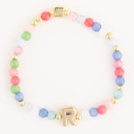 Pastel matte glass beaded bracelet featuring pink green blue and white beads interspersed with gold accents including a prominent gold letter R charm and a small etched square bead