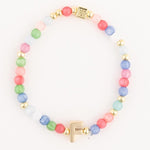 A beaded bracelet featuring vibrant multicolor glass beads in shades of pink green blue and white alternating with gold accent beads and a prominent gold initial F charm