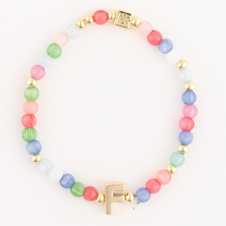 A beaded bracelet featuring vibrant multicolor glass beads in shades of pink green blue and white alternating with gold accent beads and a prominent gold initial F charm