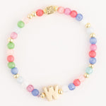 A colorful beaded bracelet featuring an array of pastel pink, green, blue, and white beads, interspersed with small gold accent beads, a prominent gold letter W, and a square gold clasp with a star-like etched design