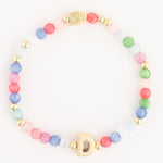Photograph of a vibrant beaded bracelet featuring an initial gold D charm small gold spacer beads and a mix of pastel pink blue green and coral round beads with a square embossed gold clasp