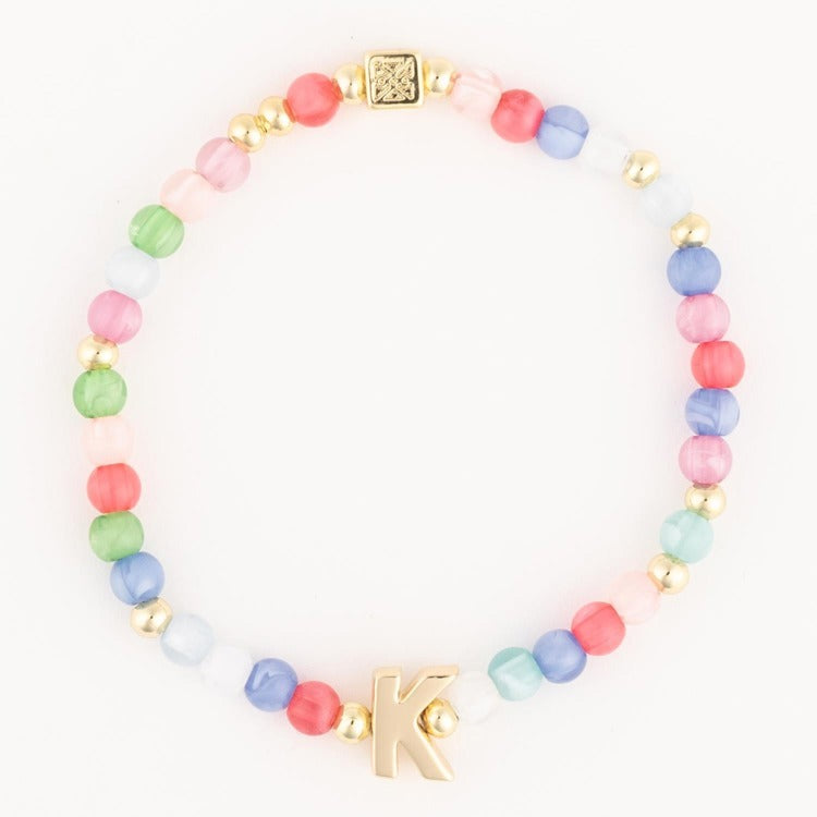 Jewelry bracelet featuring a strand of round multicolor pastel beads including pink, green, blue, coral, and white, interspersed with small gold accent beads, a square gold charm with an intricate pattern, and a prominent gold initial K charm