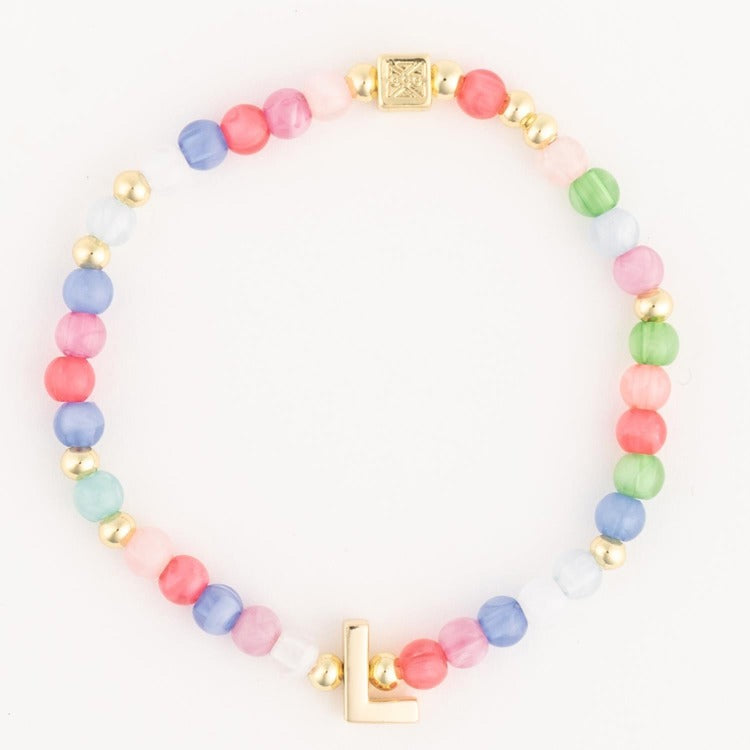 A colorful beaded bracelet featuring pastel pink, blue, green, white, and coral beads interspersed with gold accent beads, a central gold square charm with an intricate emblem, and a gold initial L charm
