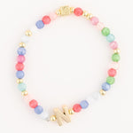 Beaded bracelet featuring pastel multicolored round beads, gold-toned spacer beads, a shiny gold letter N charm, and a small square gold charm with an etched cross design
