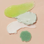 Photograph of various cosmetic product swatches on a beige background including a shimmering lime green gel a thick pale mint clay mask a smooth white cream and a pile of granulated teal exfoliating salts