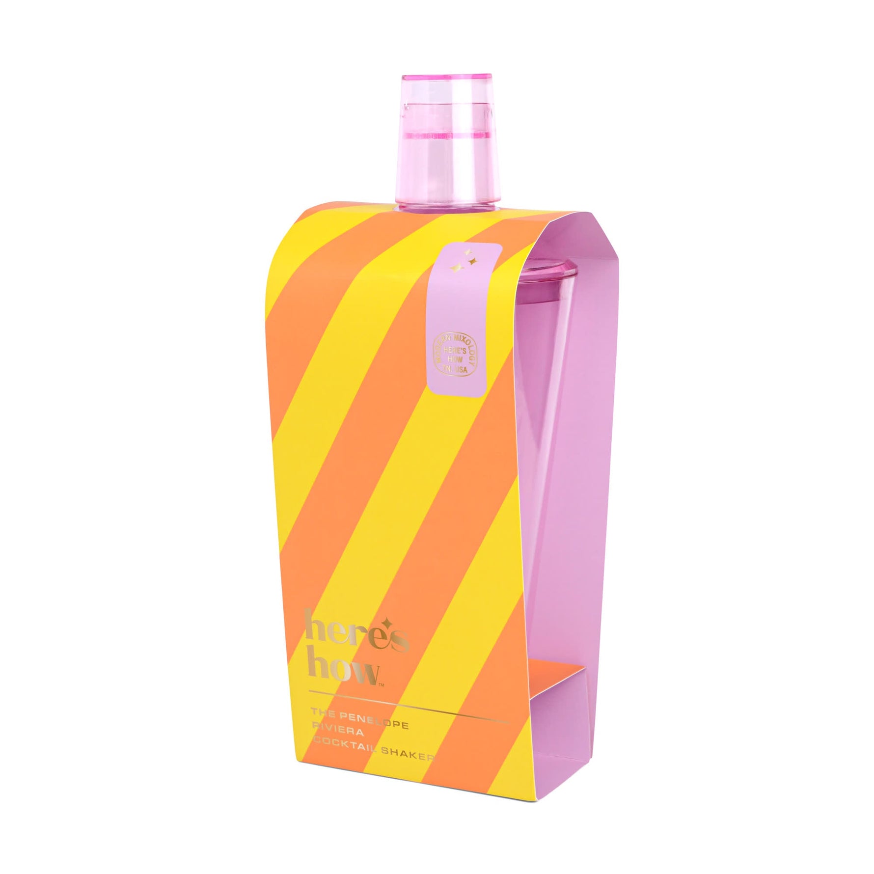 A transparent pink Penelope Riviera cocktail shaker from Here's How, displayed in its striking orange and yellow diagonally striped packaging with gold text