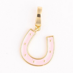 Gold-tone jewelry charm in a lucky horseshoe shape featuring pale pink enamel, small raised gold dots, and a top bail