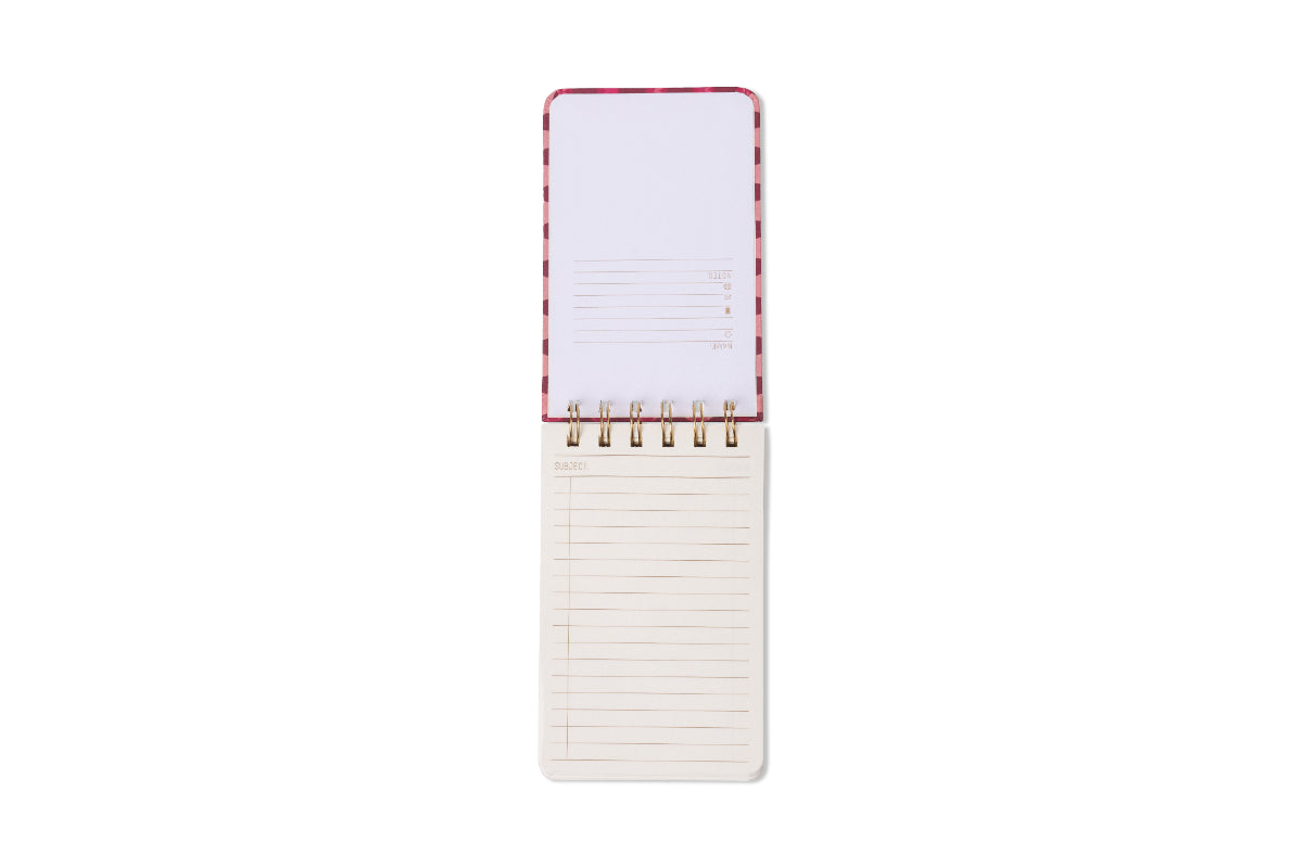 Photograph of an open spiral notebook featuring a pink and red patterned cover, gold spiral binding, a top memo page with fields for notes and messages, and a lined bottom page with a subject heading