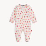 Product photograph by Magnetic Me of a white baby magnetic sleepsuit covered in a playful heart pattern of pink orange and lilac with pink ribbed trim and a rainbow interior collar detail