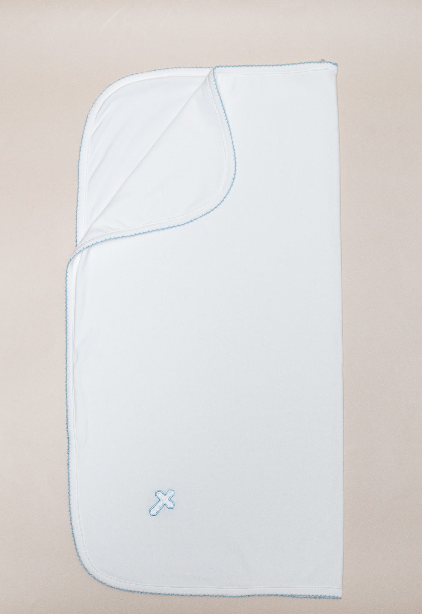White baby blanket with light blue scalloped trim and an embroidered cross symbol