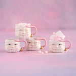 Four Santa Claus shaped mugs with pink accents filled with marshmallows on a pink background