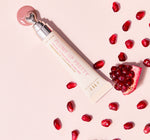 Farmhouse Fresh Plump Up Pretty Peptide Lip Treatment Blush Tint tube with a heart-shaped applicator dispensing a pink dollop, alongside vibrant red pomegranate seeds and a cut pomegranate slice on a light pink background