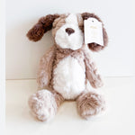 Fluffy brown and white plush puppy toy with long floppy ears sitting on a white background, featuring a heart-shaped nose and a product tag reading "meet TEDDY THE PUPPY" on its ear