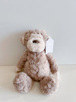 Fluffy light brown and beige stuffed monkey toy with a white tag reading meet FELIX the MONKEY sitting on a white surface