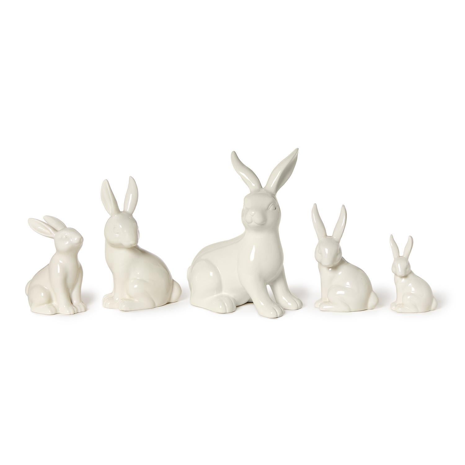 Five white ceramic bunny figurines of varying sizes are displayed on a white background featuring glossy finishes and upright ears