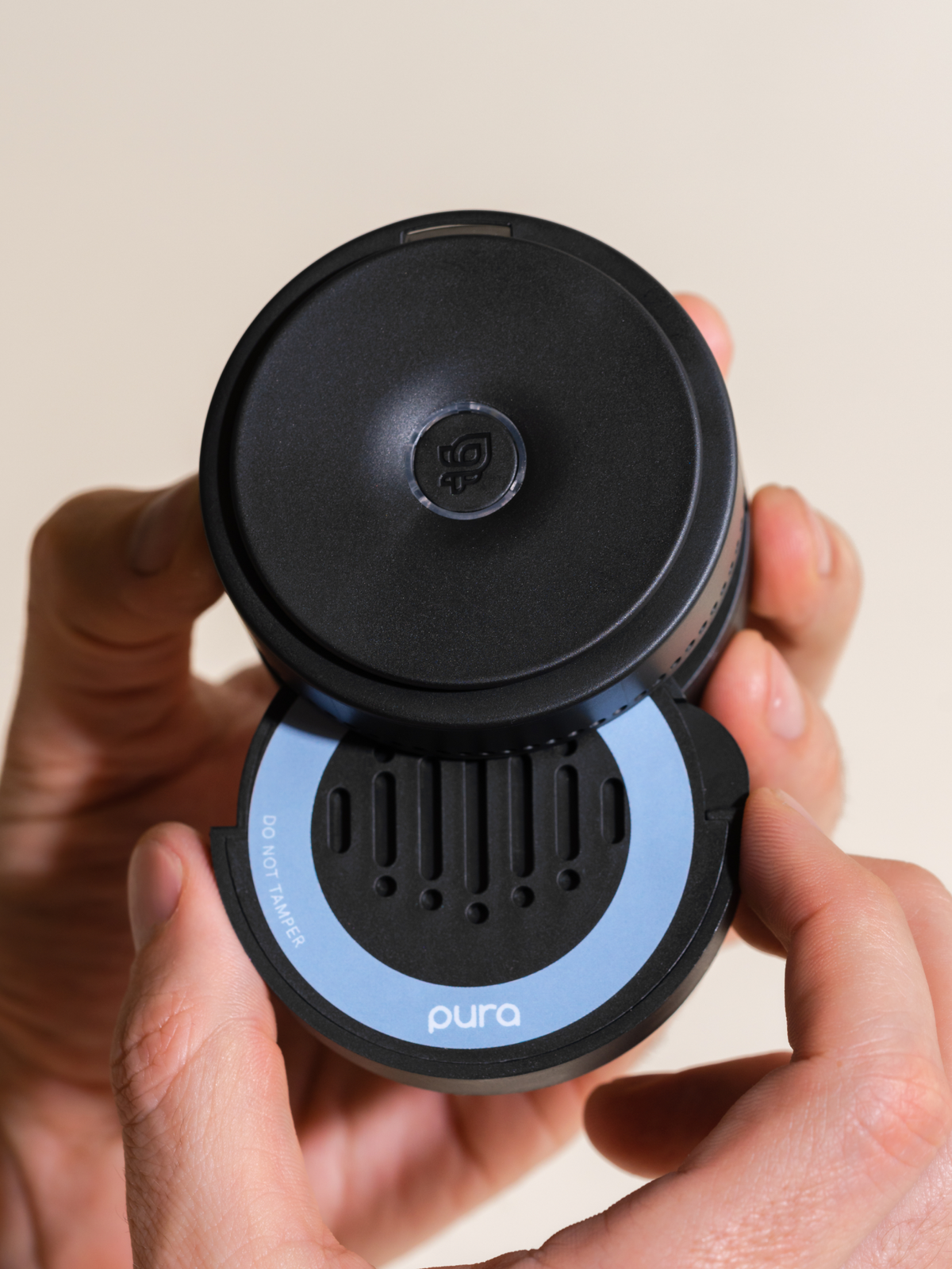 Hand holding a black car fragrance diffuser with a blue ring