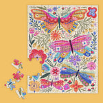 Illustrated jigsaw puzzle by Vicky Yorke of vibrant butterflies and botanical motifs on a yellow surface featuring intricately patterned pink wings, whimsical purple flowers, and a few loose pieces scattered to the left