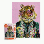 Jigsaw puzzle featuring Heather Perry's art of a stylish tiger with vibrant pink reflective sunglasses, a green faux-fur vest, and multiple chunky silver chain necklaces against a pink background, with the "Snax Size" puzzle packaging visible on the left