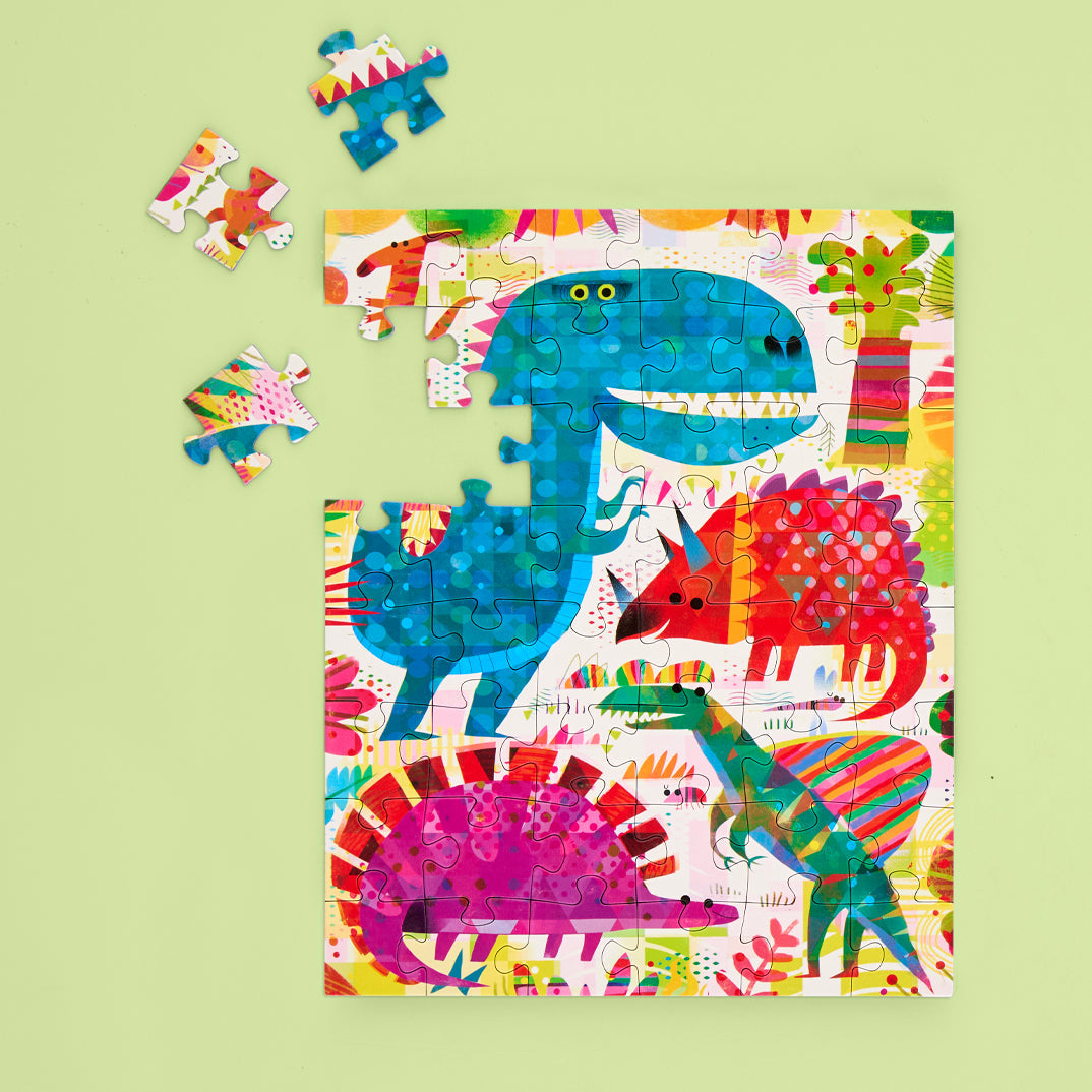 Children's puzzle featuring a vibrant prehistoric scene with a large blue T-Rex-like dinosaur, a red Triceratops, a magenta Stegosaurus, and a green striped dinosaur amidst colorful abstract foliage with three loose puzzle pieces on a light green background