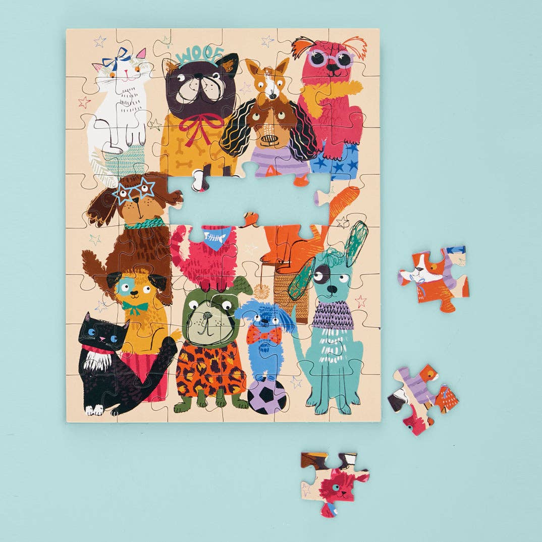 Isabelle's illustrated children's puzzle featuring a vibrant group of anthropomorphic dogs and cats wearing star glasses and leopard print, one with 'WOOF' written above its head, partially assembled on a light blue surface with three loose pieces