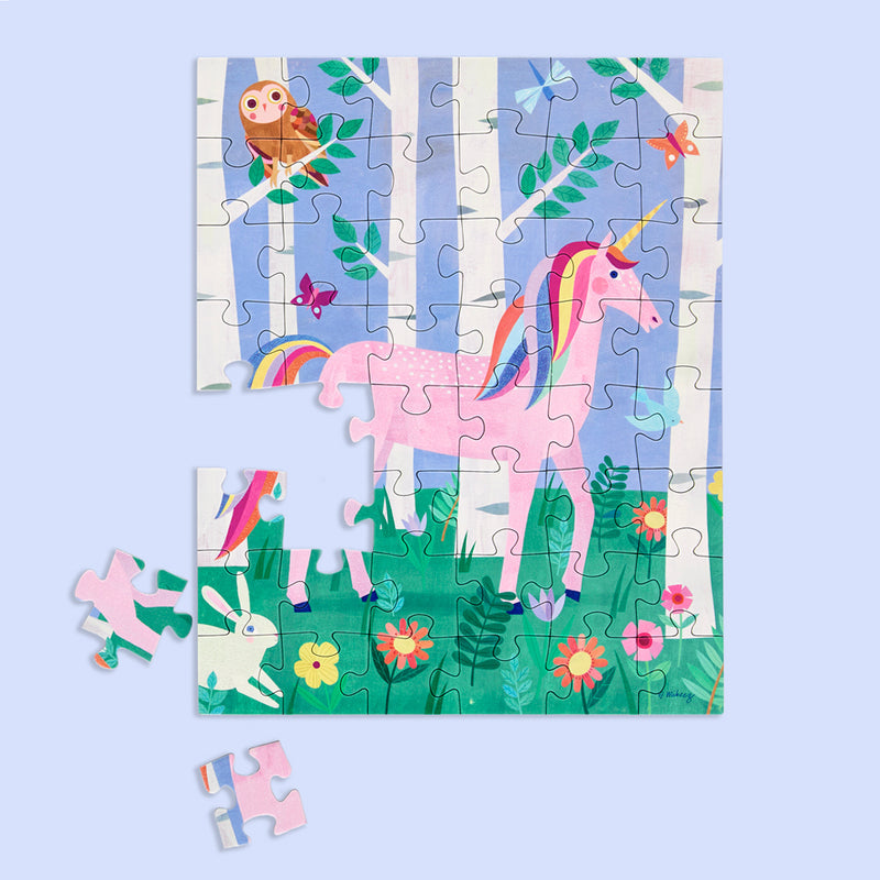 Illustrated children's puzzle featuring a pink unicorn with rainbow mane and tail in a whimsical forest clearing defined by white birch trees, an owl, a white rabbit, and vibrant wildflowers