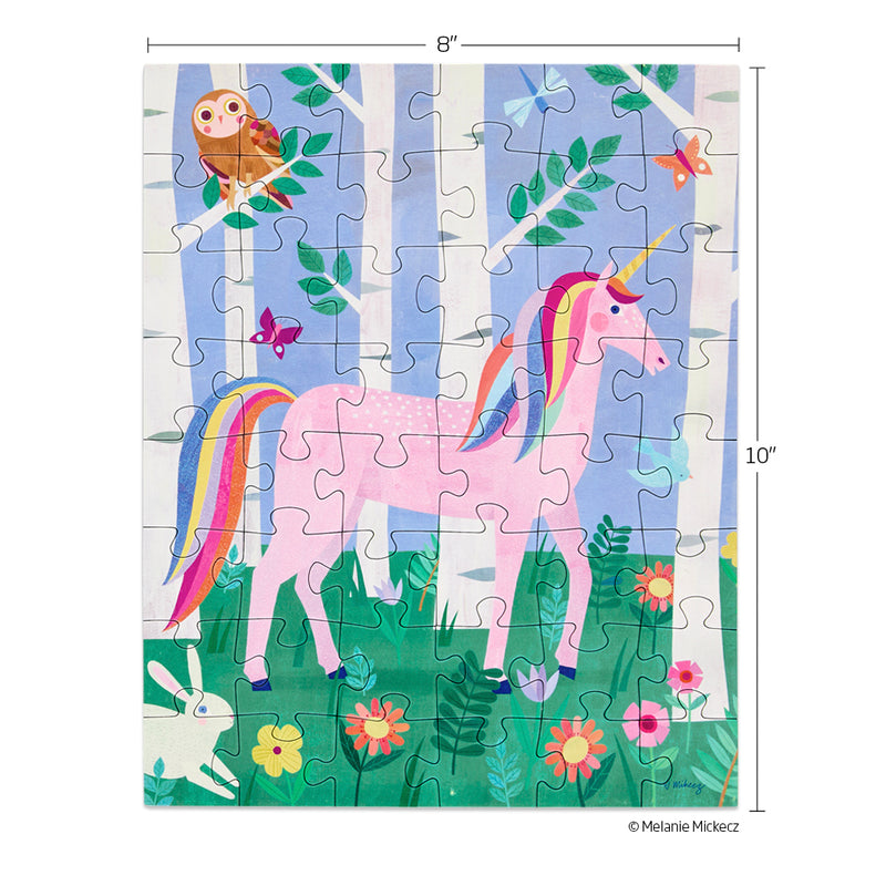 Children's puzzle by Melanie Mickecz featuring a pink unicorn with a rainbow mane and tail standing in a magical birch tree forest surrounded by a brown owl, white bunny, and colorful wildflowers
