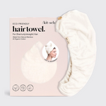 Product photography by Kitsch of a cream eco-friendly hair towel made from natural bamboo and organic cotton with a wooden button closure next to its pink packaging featuring a smiling model wearing the towel and icons for sustainable packaging and woman-owned business