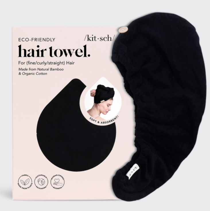 Product photography of a black Kitsch Eco-Friendly Hair Towel made from Natural Bamboo and Organic Cotton, with a wooden button closure, shown next to its light pink packaging featuring the brand name and a small image of a woman wearing the towel