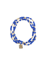 A multi-strand bead bracelet featuring vivid royal blue beads interspersed with shiny gold beads and a square gold charm with a geometric knot design on a white background