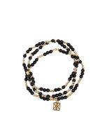 A multi-strand beaded wrap bracelet with alternating glossy black and small golden beads featuring a rectangular gold charm with an intricate geometric cut-out pattern