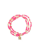 Jewelry triple-strand beaded bracelet on white background featuring vibrant pink beads interspersed with small gold beads and a square gold charm with an intricate geometric design