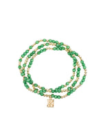 A three-strand beaded bracelet featuring alternating green malachite-like beads and small gold-tone spacer beads with a rectangular gold charm engraved with an X symbol