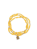Jewelry multi-strand bracelet featuring polished honey-yellow gemstone beads interspersed with small gold accent beads and a square gold charm detailed with an intricate black geometric symbol