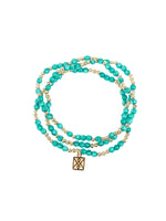 Multi-strand beaded bracelet featuring lustrous teal blue-green beads interspersed with small gold accent beads and a square gold charm with an intricate knot pattern on a white background