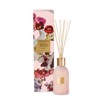 Glasshouse Fragrances Radiance in Bloom Tuberose & Orchid reed diffuser featuring a frosted pink bottle with a gold top and natural reeds next to its pink box adorned with vibrant orchid illustrations and striking red lips