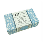 Product photo of m + BATH & BODY Hand-Crafted Bar Soap with shea butter in a light blue box adorned with white snowflake patterns featuring a white paper sleeve displaying the M logo and a blue oval 53 RELAXATION sticker all set against a white background
