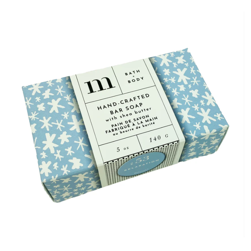 Product photo of m + BATH & BODY Hand-Crafted Bar Soap with shea butter in a light blue box adorned with white snowflake patterns featuring a white paper sleeve displaying the M logo and a blue oval 53 RELAXATION sticker all set against a white background