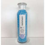 Photograph of Mixture brand clear glass bottle filled with bright blue soothing sea salt soak crystals featuring a white label with "53 Relaxation" in lavender text on a minimalist white background