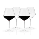 Studio photograph of four elegant stemmed wine glasses on a white reflective surface two filled with deep red wine and two empty