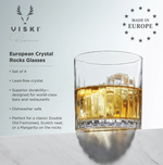 Product photograph by VISKI Reserve featuring a clear European crystal rocks glass with a ribbed design filled with amber liquid and ice, elegantly displayed on a white marble surface, underscored by the 'Made in Europe' star logo
